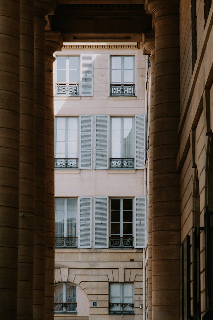 Vue verticale des fenêtres à volets d'un bâtiment classique encadrées par des colonnes, mettant en valeur l'architecture urbaine.